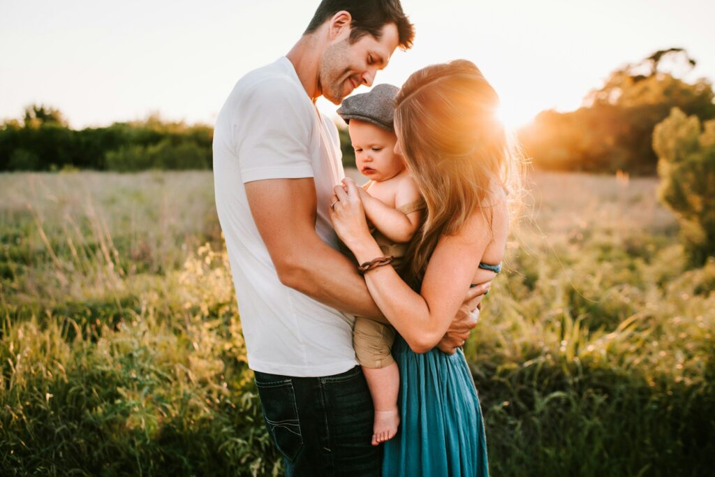 Mom and dad hugging child in meadow