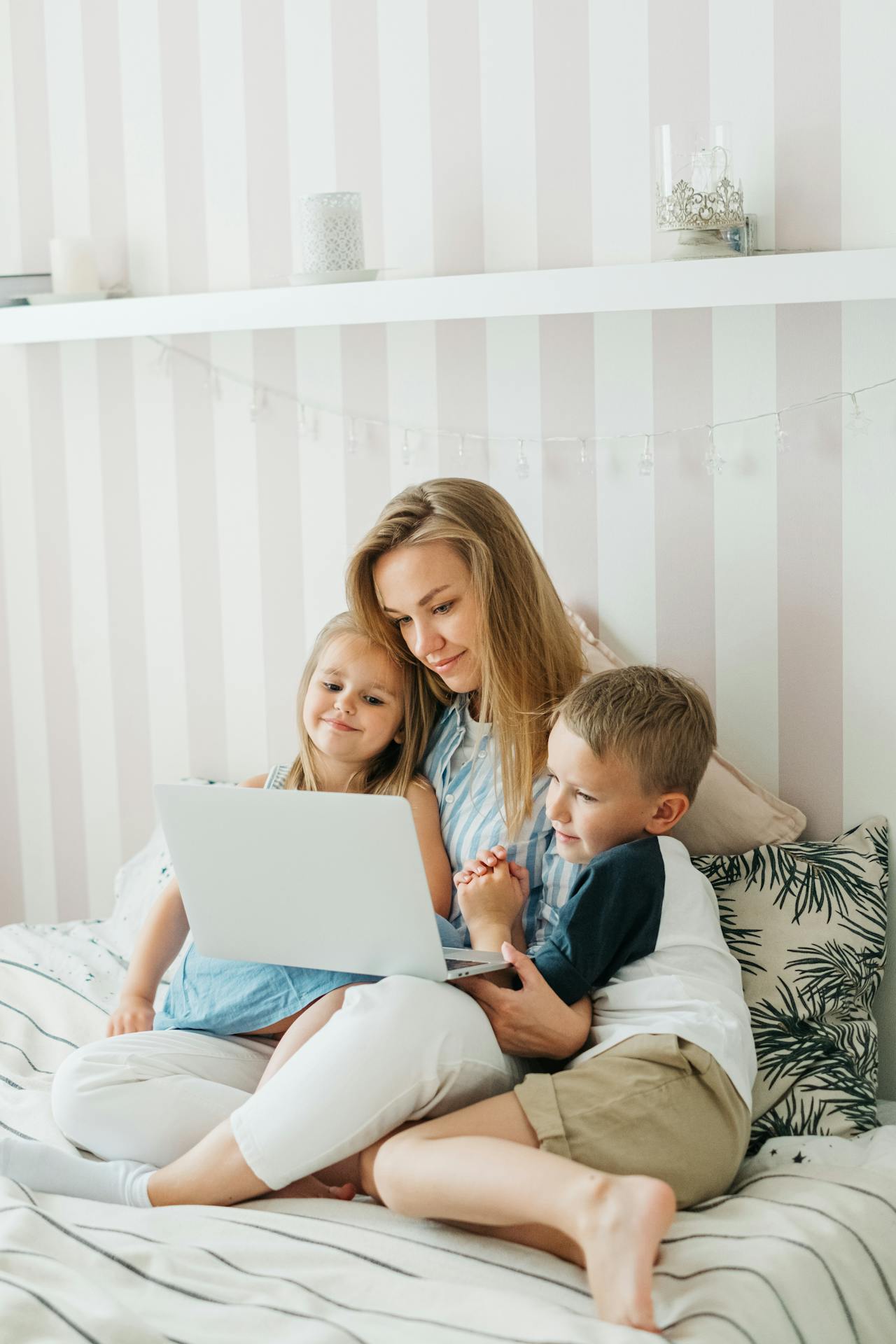 A mom with her son and daughter on a bed looking at a laptop