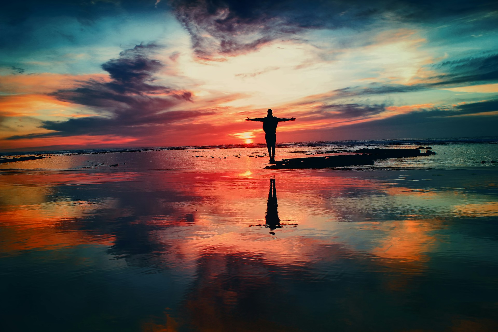 Person standing on a rock by body of water at sunrise